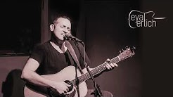 אייל ארילך עומד ומנגן בגיטרה, לפניו מיקרופון